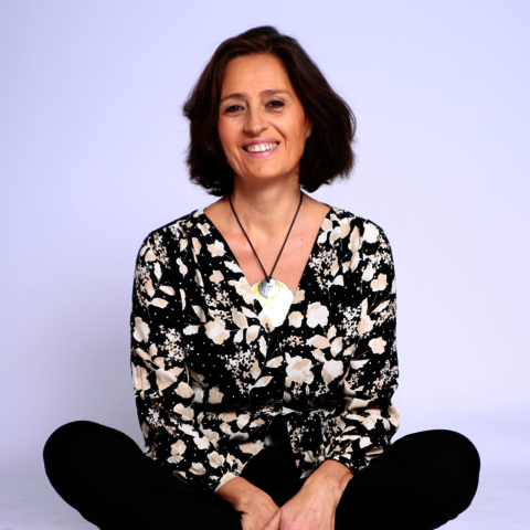 Femme souriante assise en Sukkasana, habillée en pantalon noir et haut beige et noir