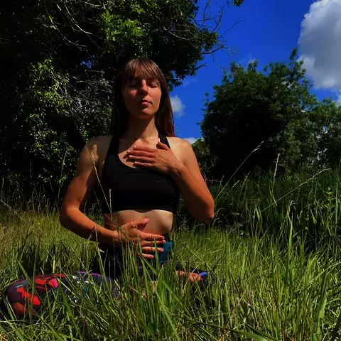 Professeure de yoga assise en pratique de respiration consciente dans la nature