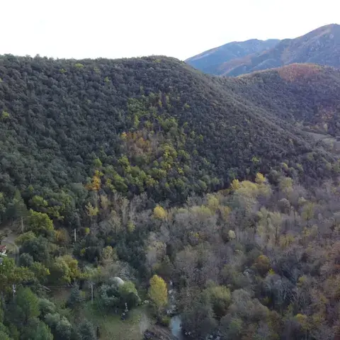 Vue panoramique plongeante sur un domaine privé de 9 hectares niché dans la verdure, comprenant un grand chalet de prestige, un mas en pierre, une piscine et une rivière sauvage en bordure de propriété.