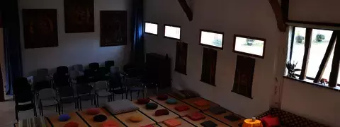 Grande salle pour cours de yoga, séminaires et stages bien-être Grande salle de 100m2 disposant de tatamis, écran projecteur, paper board, accès wifi. De plein pied, donnant sur les jardins du domaine.
