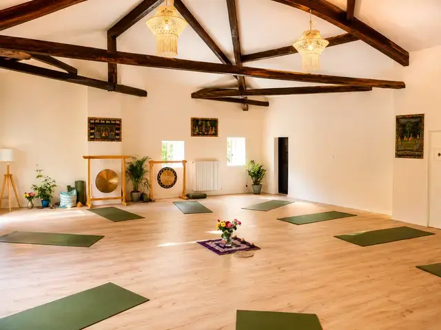 Salle de yoga lumineuse de 85 m² au Château de Shanti Lake en Ariège, avec poutres apparentes, parquet en bois et tapis de yoga disposés pour une retraite.
